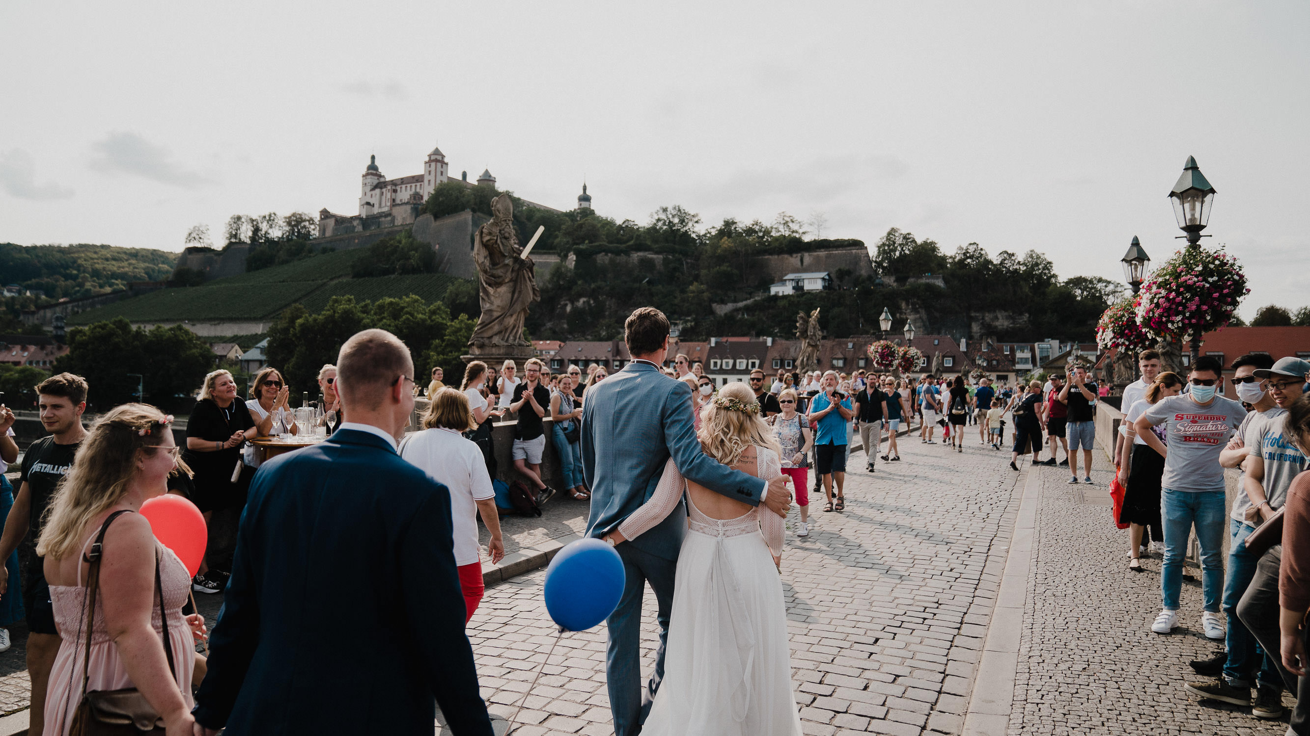 Das Brautpaar läuft über die Alte Mainbrücke in Wuerzburg. Die Festung Marienberg im Hintergrund. Fotografiert von Hochzeitsfotograf Axel Link