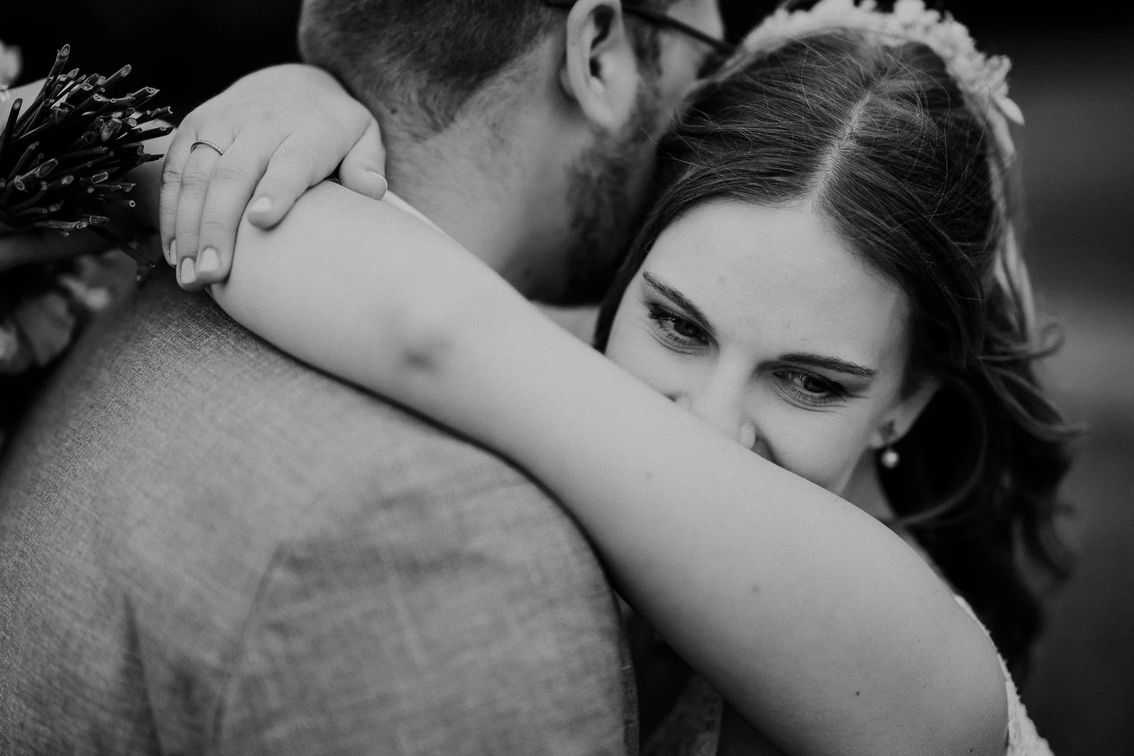 Hochzeitsfotograf Wuerzburg 17 Eine Nahaufnahme in Schwarz-Weiß von einer Braut, die ihren Partner während der Hochzeit umarmt. Sie lächelt sanft, ihr Verlobungsring ist sichtbar, während das Gesicht ihres Partners abgewandt ist - perfekt eingefangen vom Hochzeitsfotograf Würzburg.